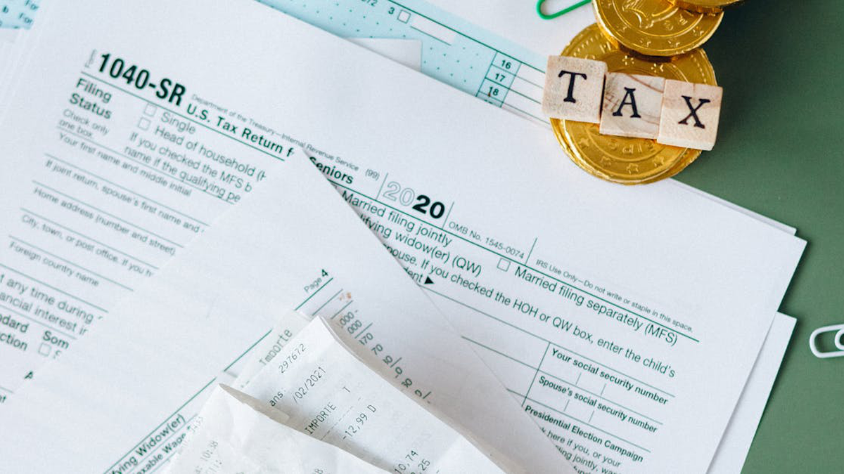 Picture Of Tax Documents Spread On A Desk With Two Gold Coins On Top And Stickers Spelling TAX